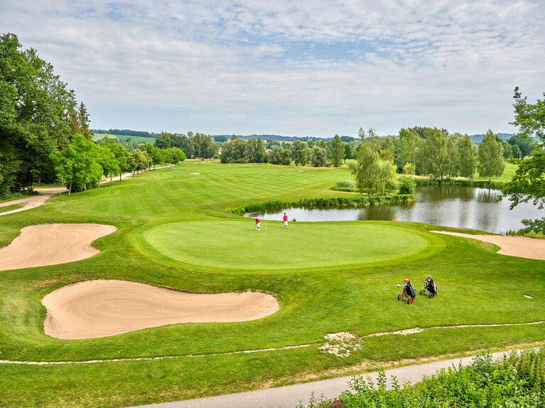 Eindrucksvoller Golfplatz mit verschiedenen Sandbunkern und einem Teich im Hintergrund.
