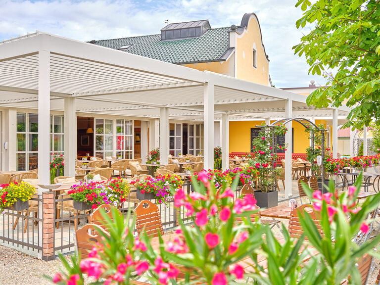 Eine sonnige Terrasse mit gemütlichen Sitzgelegenheiten, umgeben von bunten Blumen und einer freundlichen Atmosphäre.