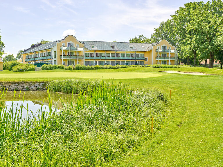 Das gelbe Hotelgebäude mit Balkonen, umgeben von Grün und einem kleinen Teich, in der Nähe vom Luftkurort Bad Griesbach.