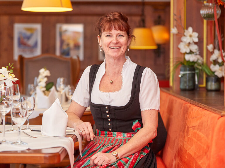 Lächelnde Gastgeberin im traditionellen Dirndl in einem gemütlichen Restaurant.