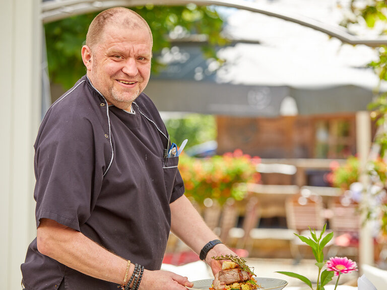 Koch serviert ein Gericht im Freien. Jobs bei Bad Griesbach bieten kreative Möglichkeiten in der Gastronomie.
