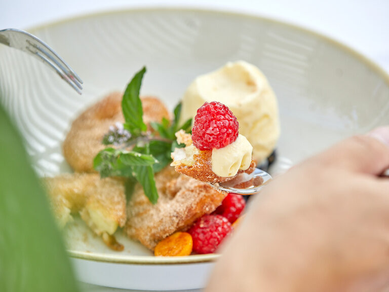 Ein köstliches Dessert mit frischen Himbeeren und einer cremigen Füllung, kunstvoll auf einem Löffel angerichtet.