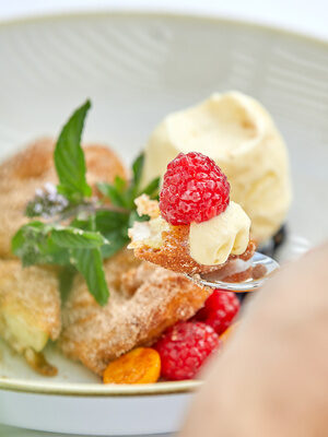 Ein köstliches Dessert mit frischen Himbeeren und einer cremigen Füllung, kunstvoll auf einem Löffel angerichtet.