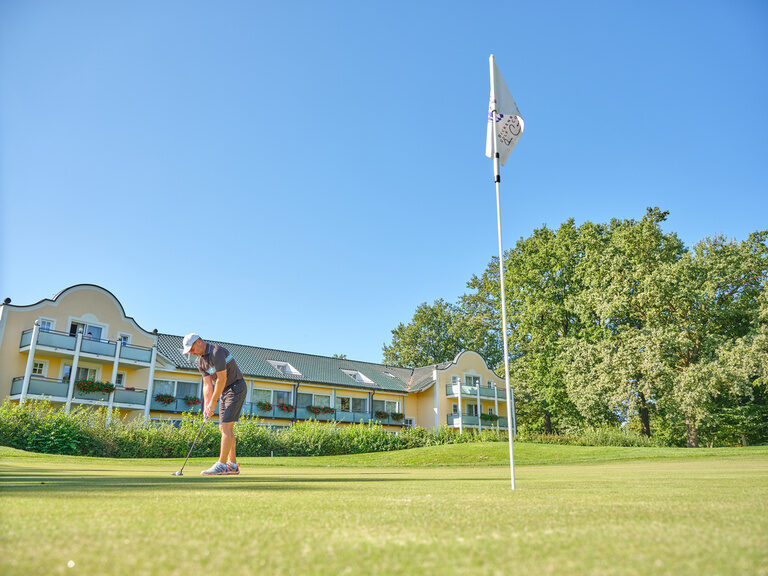 Ein Golfer beim Putten auf einem gepflegten Grün vor einem eleganten Golfhotel bei Bad Griesbach.