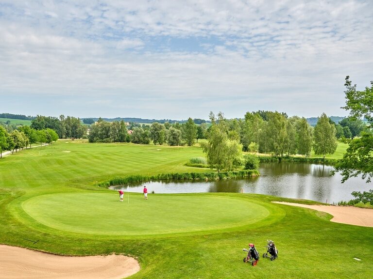 Ein weitläufiger Golfplatz mit gepflegtem Grün, Sandbunkern, einem Teich und spielenden Golfern.