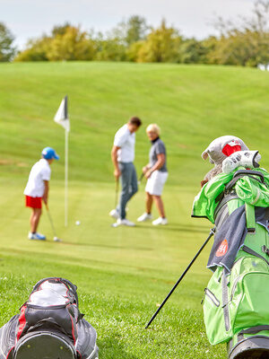 Eine Familie spielt Golf auf einem weitläufigen, grünen Golfplatz, mit dem Golfbag im Vordergrund.