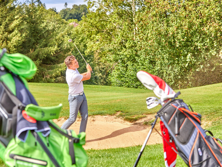 Ein Mann beim Abschlagen eines Golfballs mitten auf dem grünen Golfplatz.