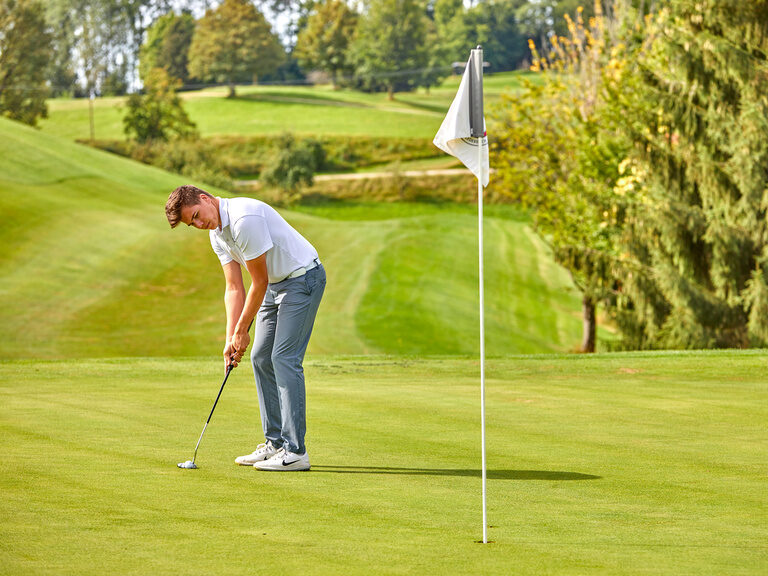 Mann beim Putten auf einem gepflegten Golfplatz mit Fahne im Hintergrund.