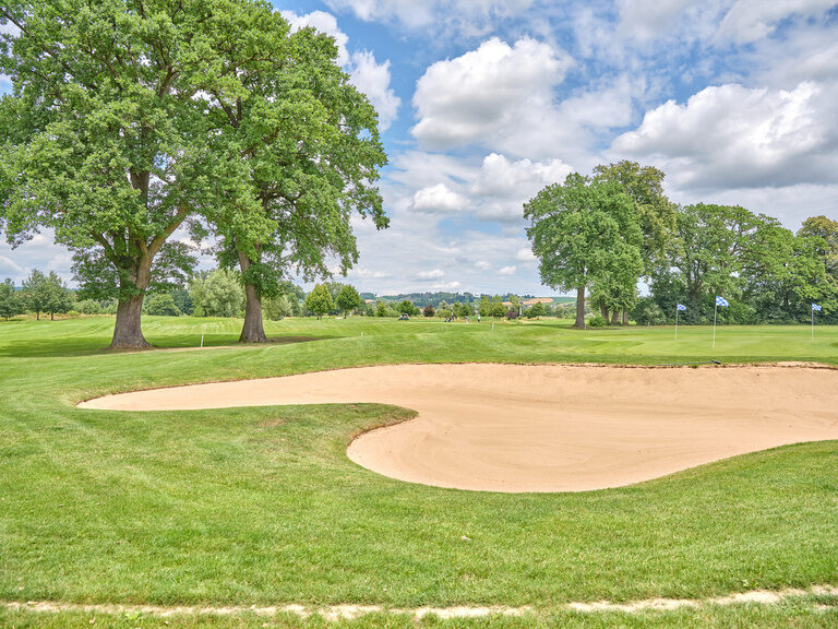 Ein gepflegter Golfplatz mit Sandbunker, umgeben von grüner Natur und einer ruhigen Landschaft.