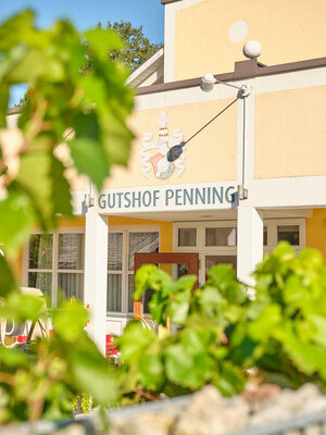 Nahaufnahme des „Gutshof Penning“-Schilds, umrahmt von Pflanzen.