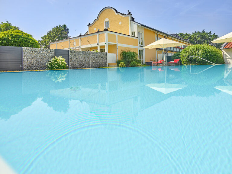 Blick über den ruhigen Pool auf ein stilvolles Hotel mit Pool in Bayern.