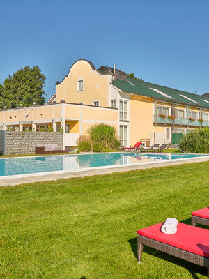 Das Hotelgebäude mit einem Swimmingpool und Liegestühlen im Vordergrund.