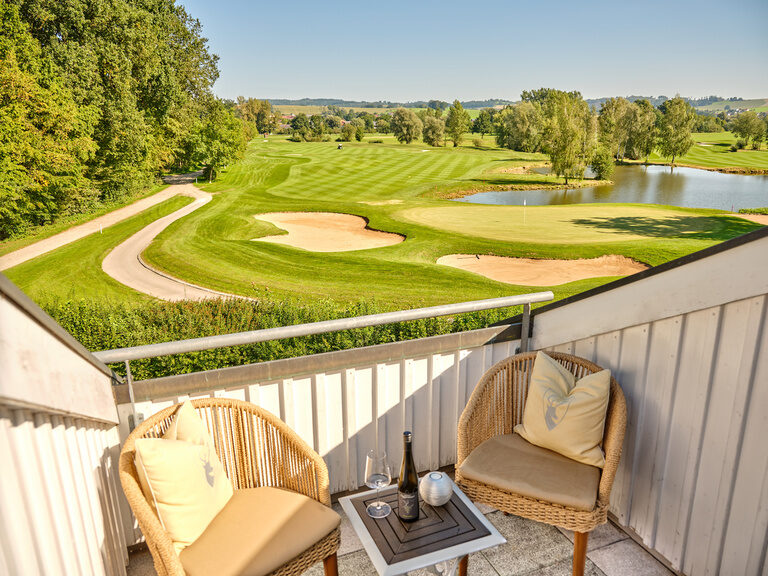 Ein Balkon mit gemütlichen Sitzmöbeln und Blick auf den Golfplatz und die Landschaft rund um den Gutshof bei Bad Griesbach.