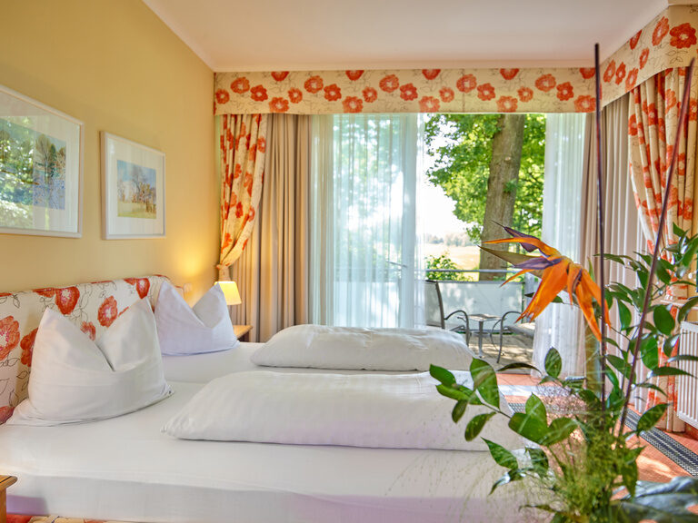 Ein helles Hotelzimmer mit Blumenmuster, großen Fenstern und Blick auf die Natur.