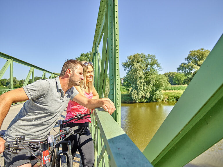 Ein Paar mit Fahrrädern genießt die Aussicht von einer Brücke während ihres Radurlaubs in Bayern.