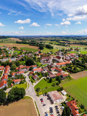 Luftaufnahme eines malerischen bayerischen Dorfes mit umliegenden Feldern und einer idyllischen Landschaft.