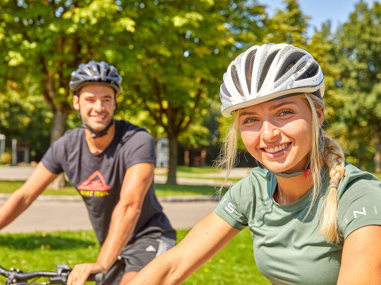 Nahaufnahme von zwei glücklichen Radfahrern mit Helmen, die ihren Radurlaub in Bayern genießen.