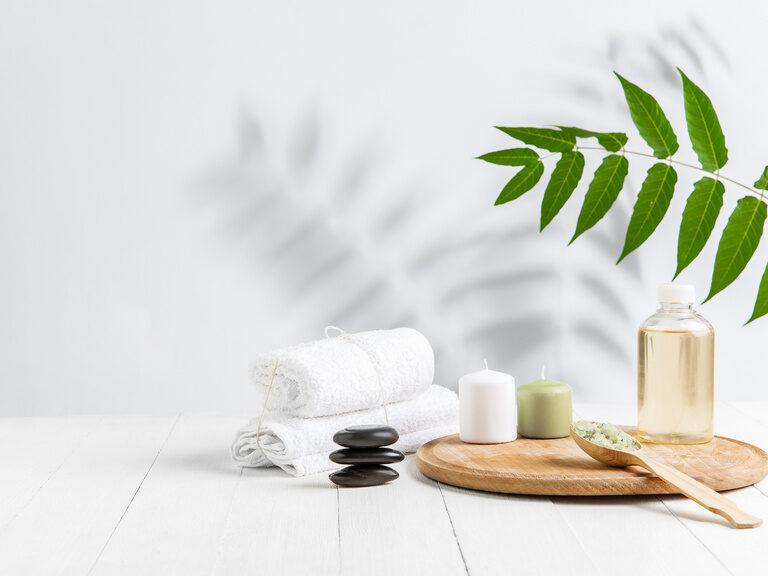 Wellness-Accessoires wie Handtücher, Steine, ätherische Öle und Kerzen auf einem Holztablett.