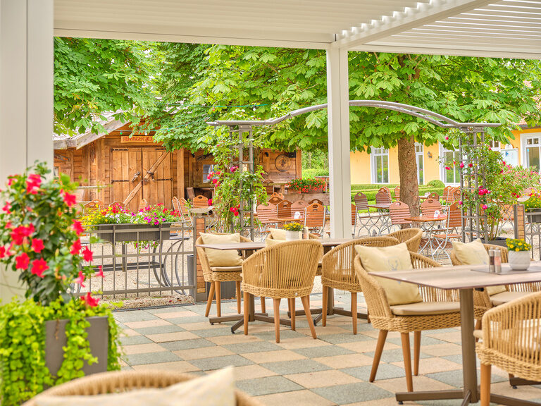Ein gemütlicher Biergarten mit schattigen Bäumen und traditionellen Holzmöbeln, ein idyllischer Ort.