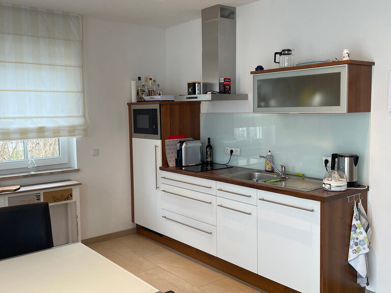 Küchenzeile mit weißen Schränken, Kaffeemaschine, Spüle und Ceranfeld.